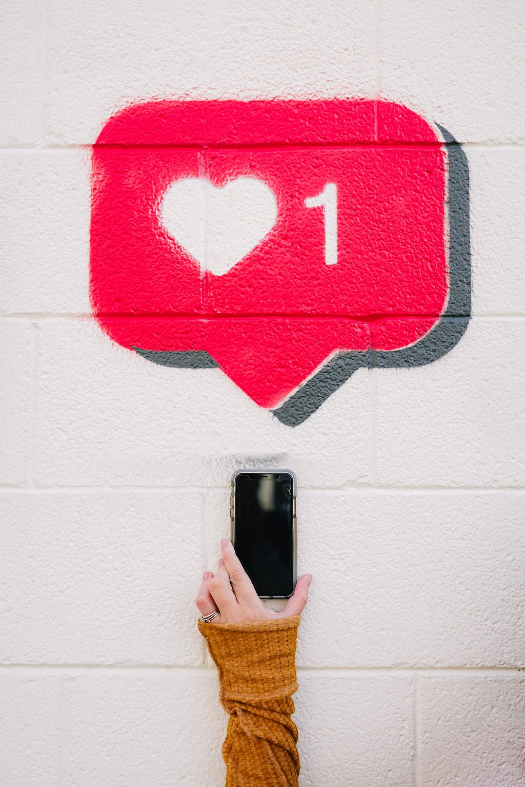 A hand is holding a mobile phone under a big red social media heart sign.