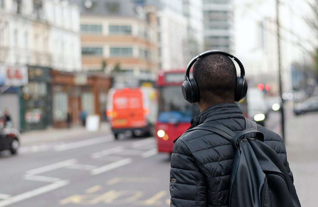 Person wearing a headset looking towards a traffic intersection. Buses and buildings are seen are in the background