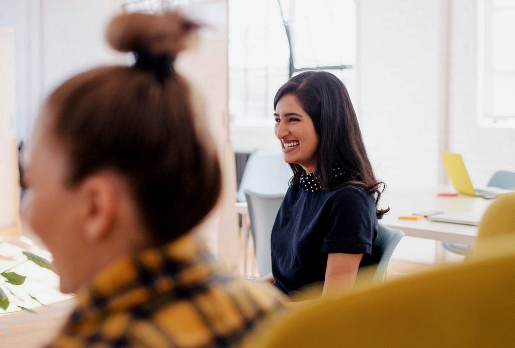 Mulheres sorrindo durante sessão de brainstorm presencial.