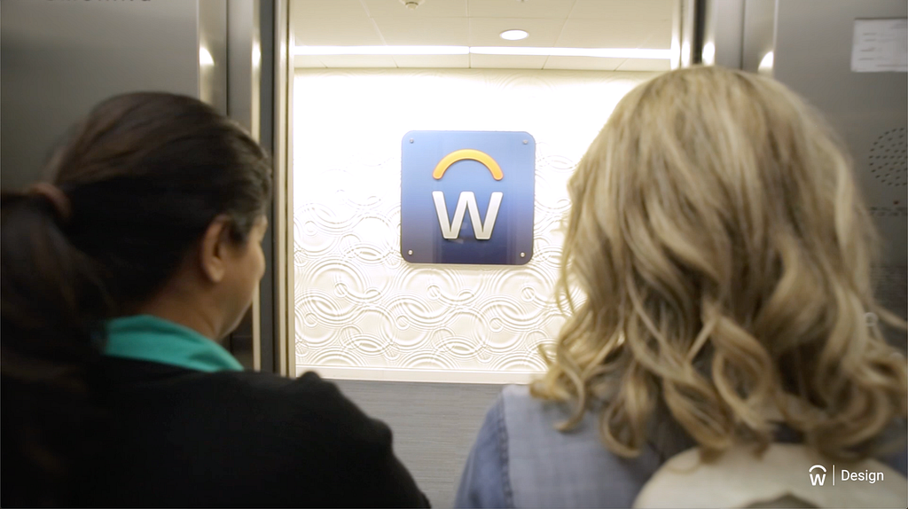 Video still of two women from the back, looking at a wall with the Workday “W” logo on it.