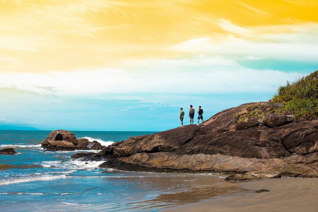 Three people on a rock overlooking the ocean