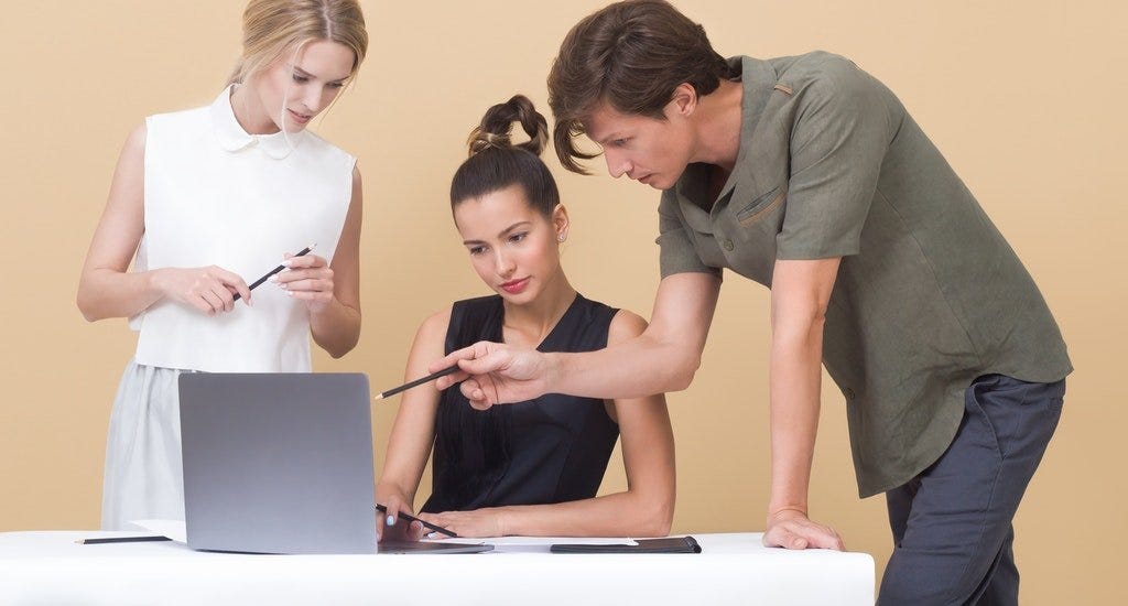 Two women and one man looking and point at a laptop