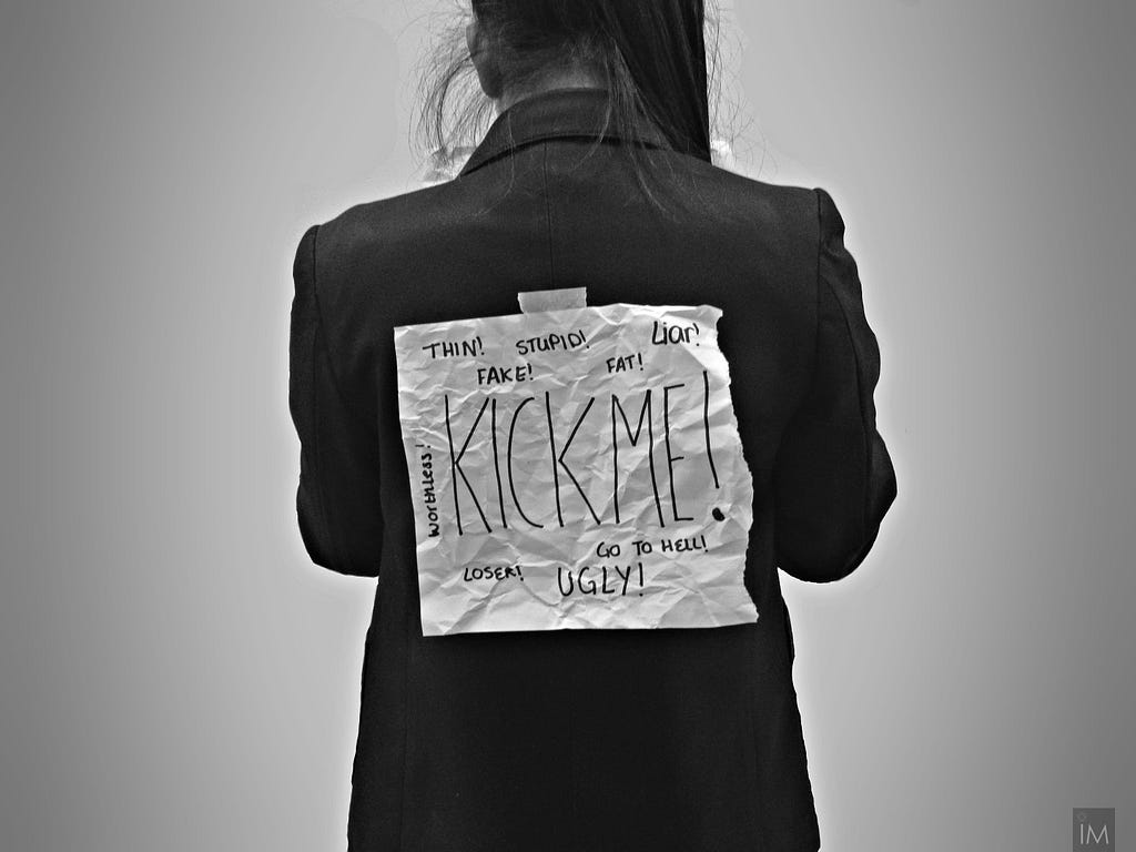 A woman standing with her back to the camera with a “kick me” sign and negative words around it.