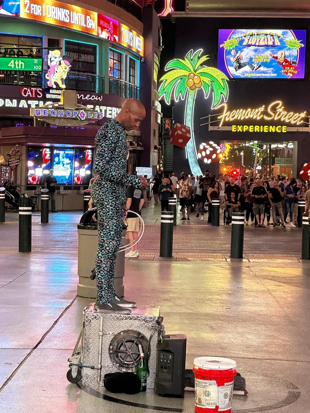 A person is performing with a microphone and speaker setup on a busy street under bright neon lights and advertisements.