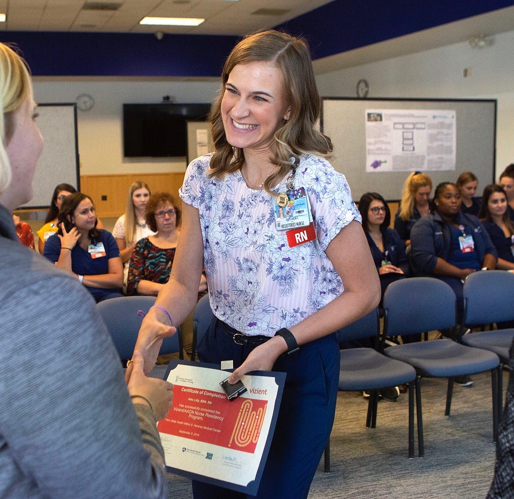 Alex Lilly shakes the hand of a mentor in her nursing uniform.