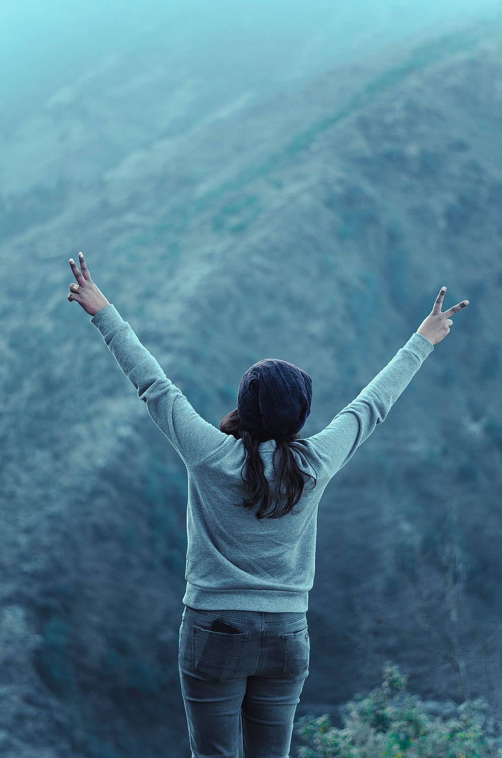A woman standing on the top of a mountain and showing the sign of victory