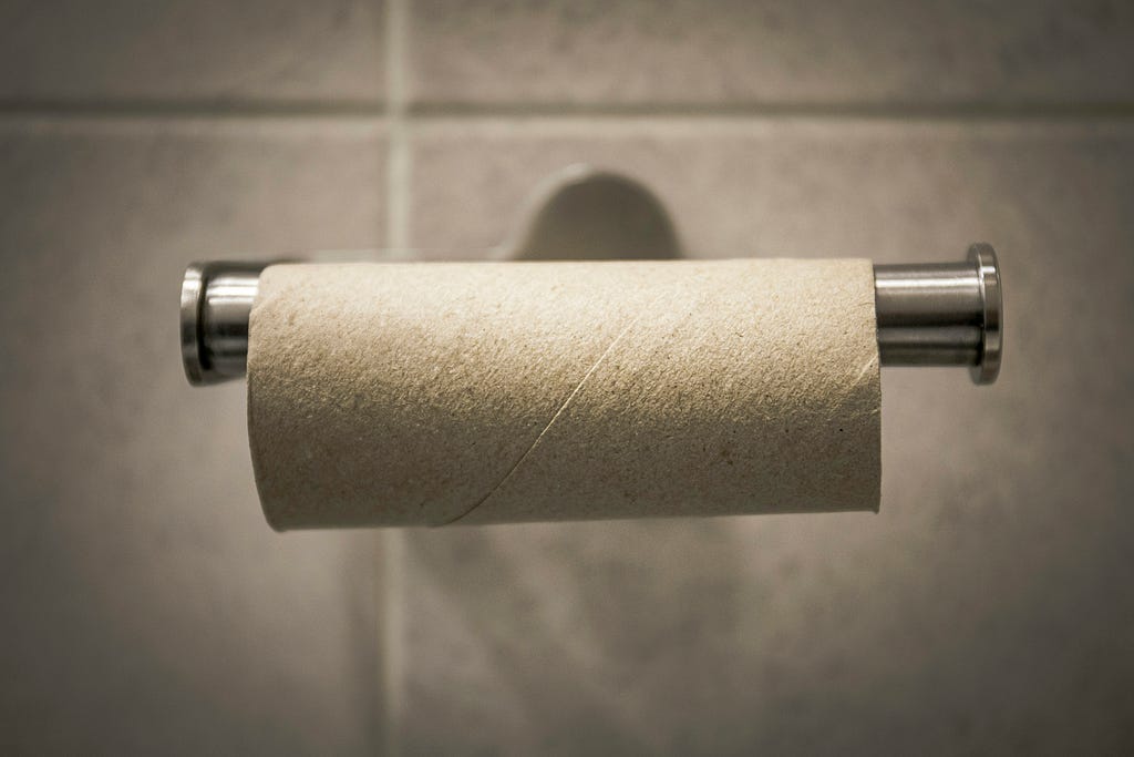 An empty cardboard roll hangs on a bathroom toilet paper dispenser — everyone’s nightmare if not noticed before — there’s no toilet paper.