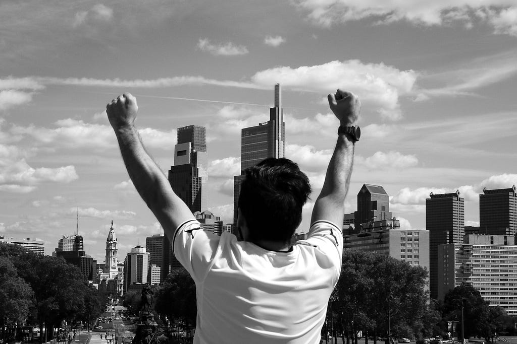 Man overlooking skyline with hands in the air