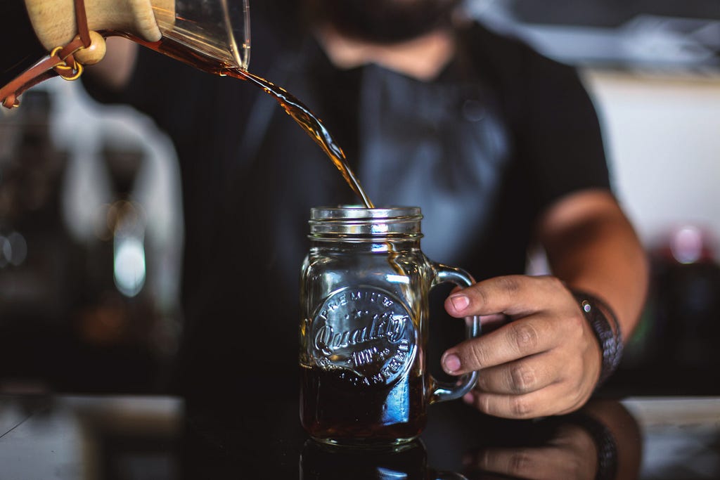 A barista  pouring cold brew coffee into a glass.