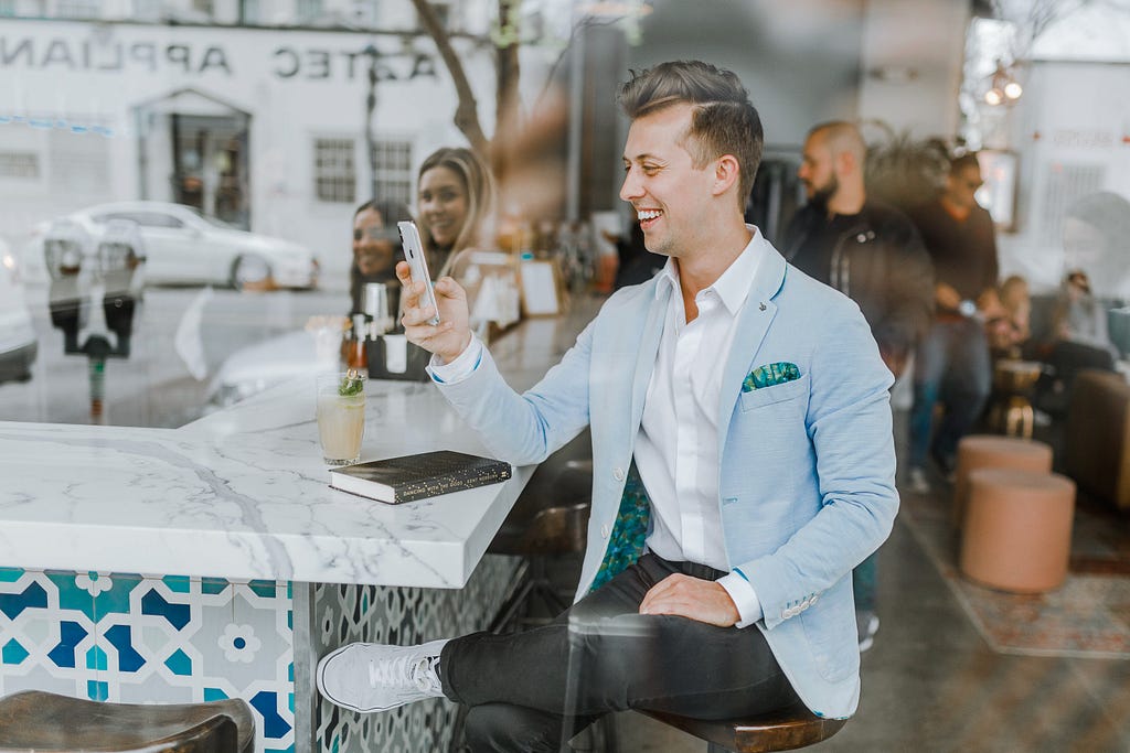 A man sitting with a phone in his hands, smilling heartily