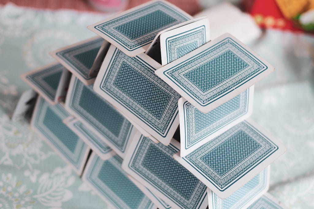 A house of blue patterned playing cards on a pale blue and white bedspread