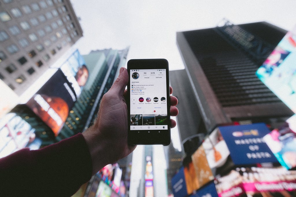 a photo of hands holding a phone displaying instagram in a city location