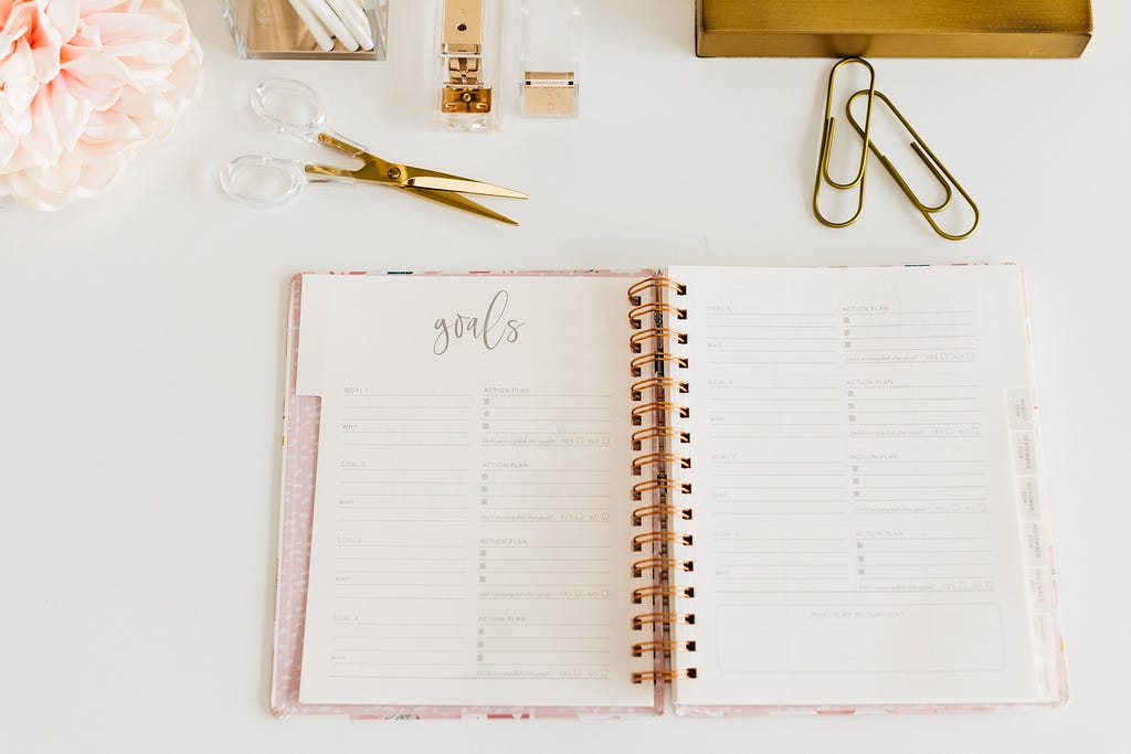 A pink journal for setting goals sits on a desk with other desk accessories.