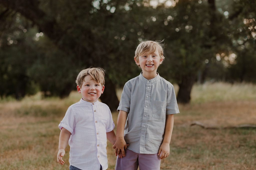 Two young boys standing outside holding hands and smiling