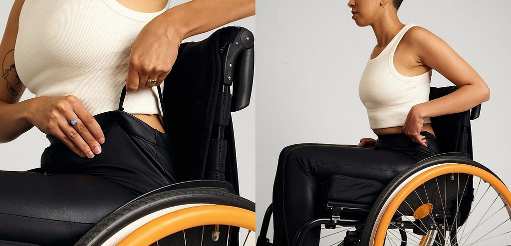 Close up image of a woman wearing a white crop top and black trousers. She is sitting in a wheelchair and pulls up her trousers by the pull up loops.