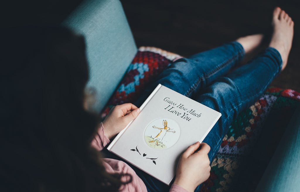 Menina sentada com um livro branco no colo. Na capa do livro há um desenho de um coelho.