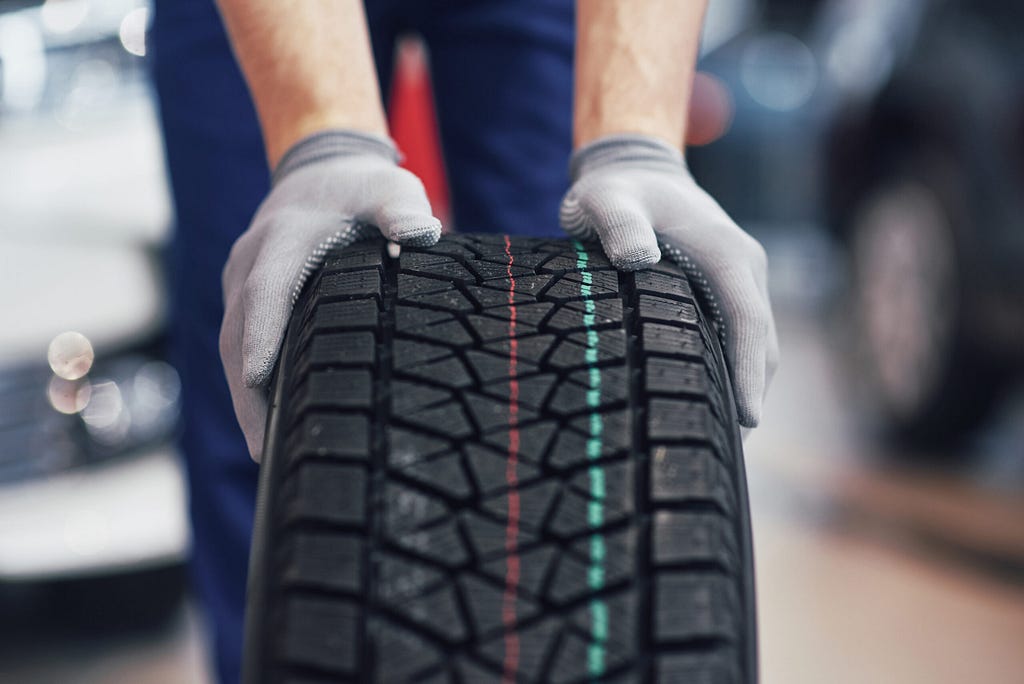 A mechanic, wearing a pair of gloves, holding a winter tire.