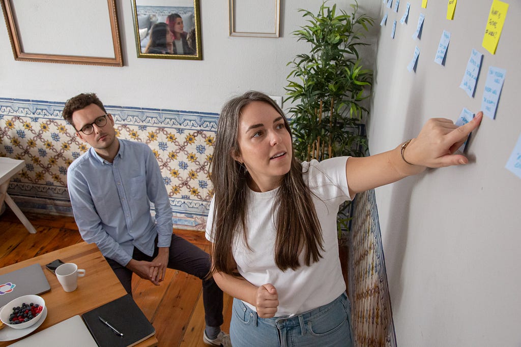 Two people look & point at a white board with various sticky notes on it