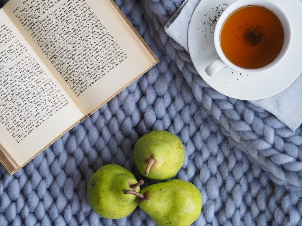 This image depicts a green fruit, a cup of tea, and a book on top of a table.