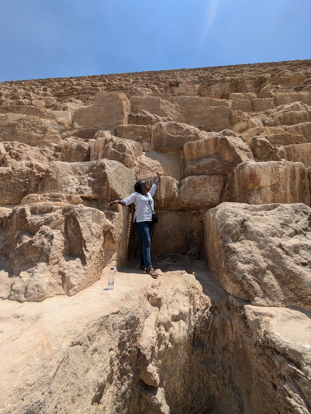The author, Amani Ali, stands on a ledge near the base of the largest of the Great Pyramids of Giza (Khufu) and motions upward.