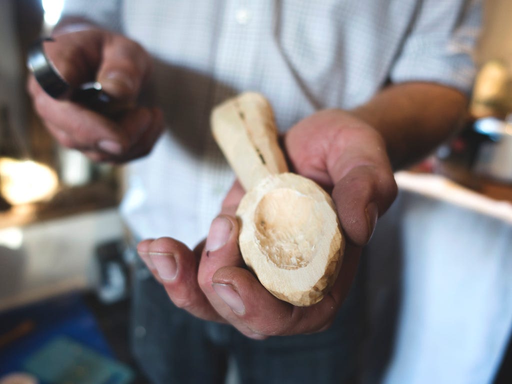The picture depicts a wood carver carving a small, oval-shaped dent into a wooden object.