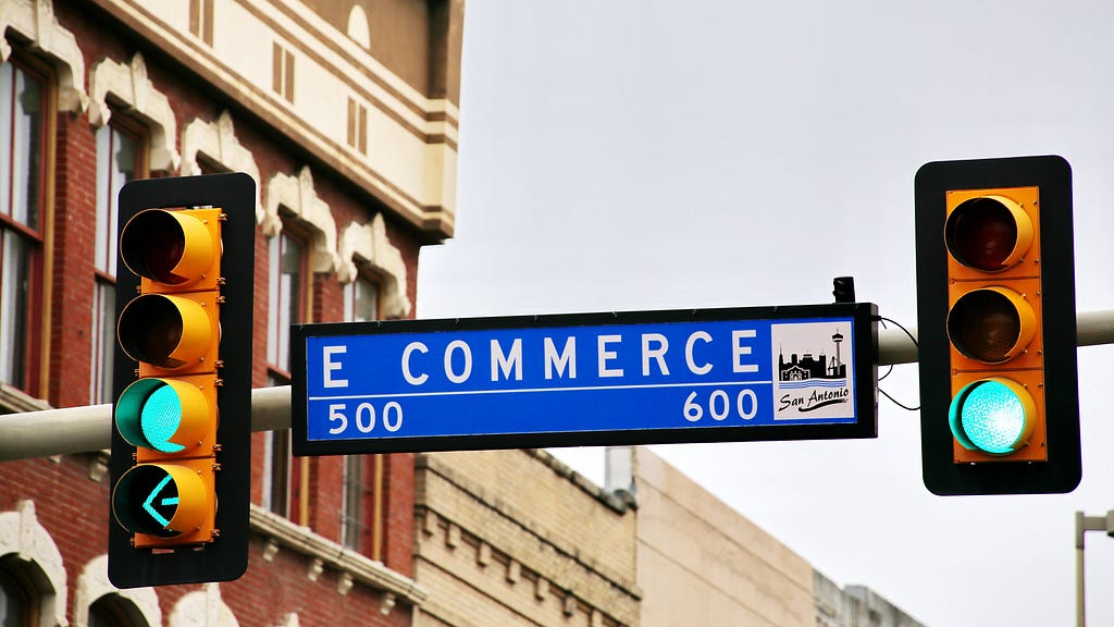 A traffic sign labeled ‘E-Commerce’ is positioned between two green traffic lights.