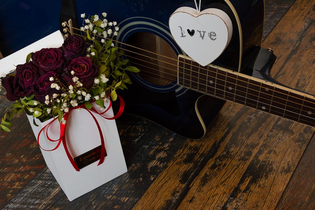 a guitar with a bouquet of roses, signifying songs that are about unrequited love