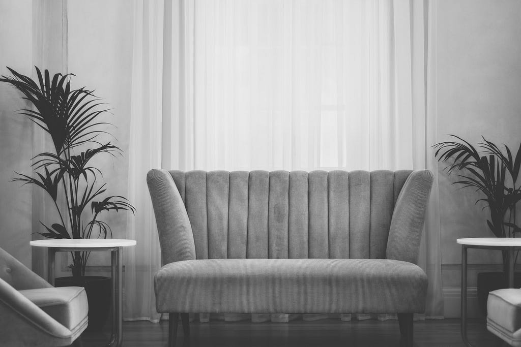 A grey-scale image of a loveseat in a living room setting