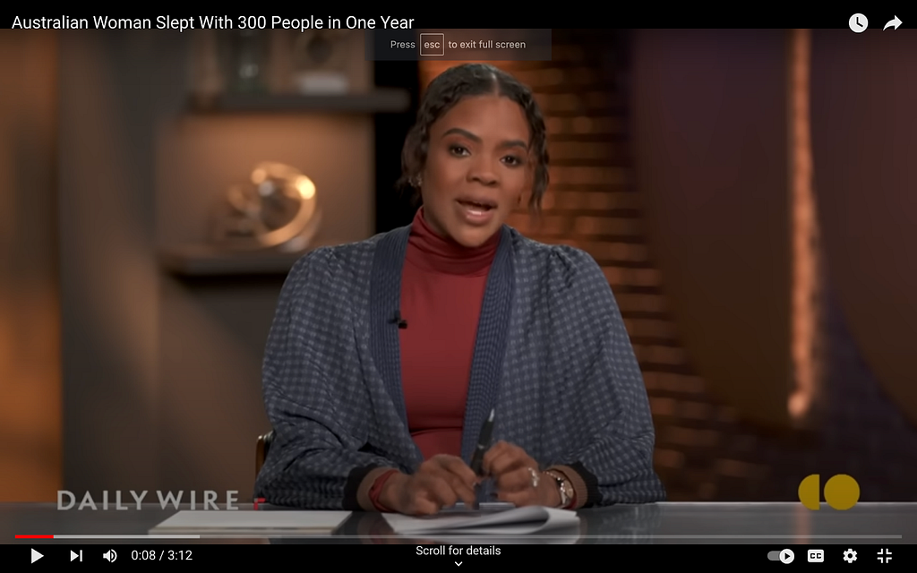 A screenshot from Candace Owens’s show on The Daily Wire. She wears what seems to be a red turtleneck under a slouchy cardigan. The cardigan is dark blue and left mostly open. It has a gingham pattern, looks cozy and could be made of wool. There’s the hint of a puff sleeve.