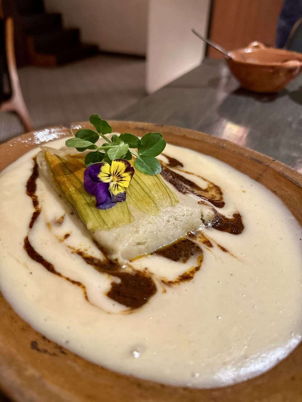 Duck Tamal decorated with flowers and sitting in a garlic cream sauce
