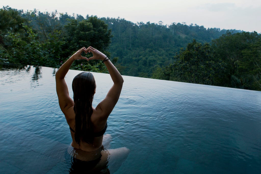 A woman in a swimming with her hands up and her finger folded into a love symbol