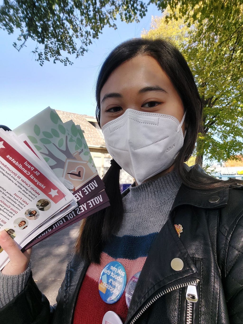 A photo of Leyen Trang wearing a face mask and holding up two sets of colorful fliers.