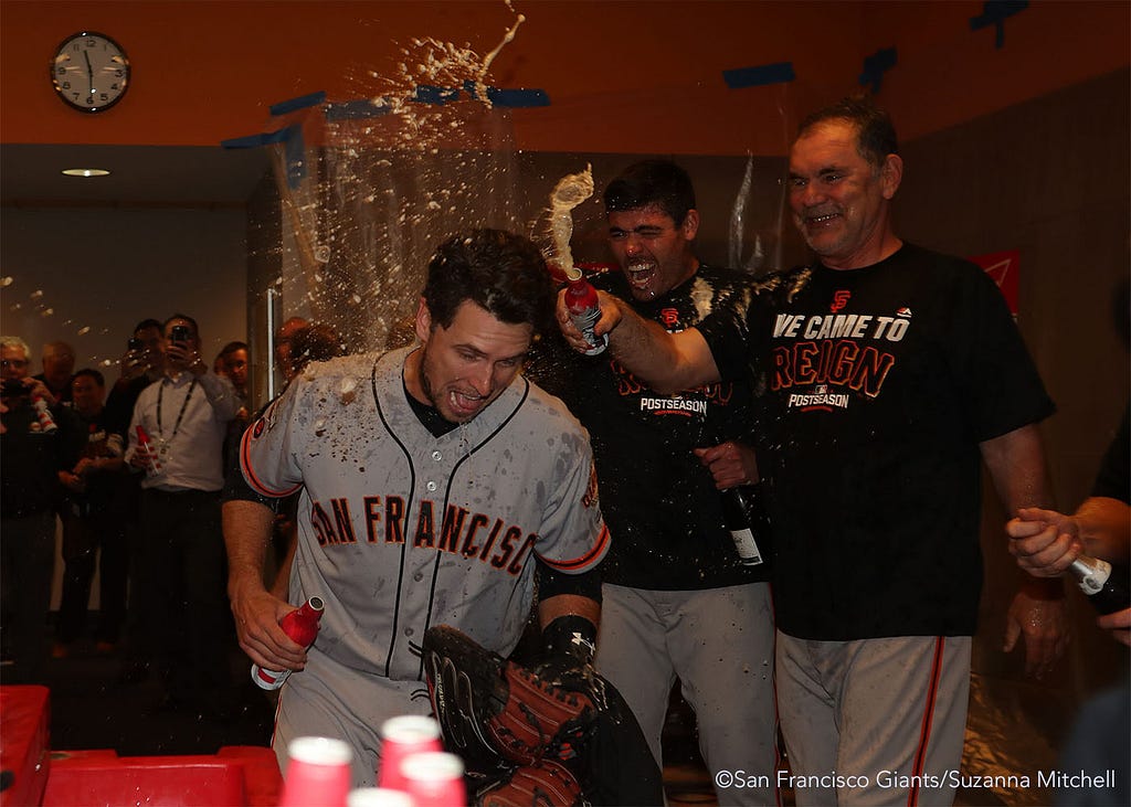 Buster Posey, Matt Moore and Bruce Bochy celebrate in the clubhouse.