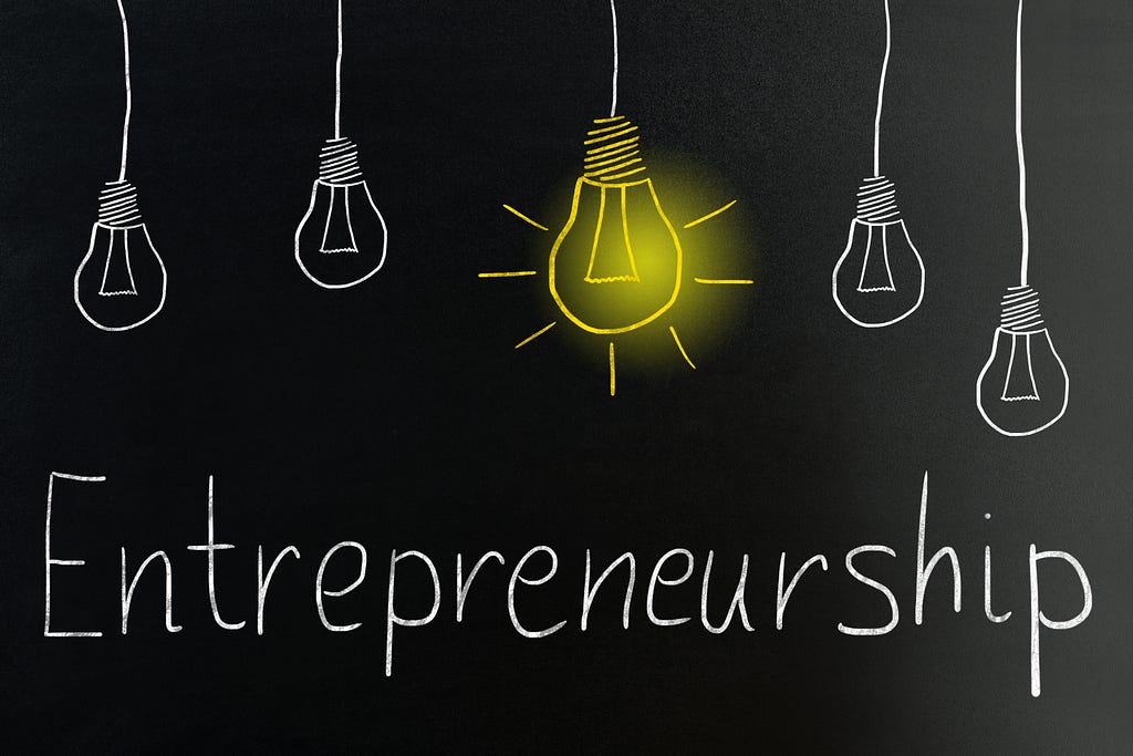 A word " Entrepreneurship " on a balck background with a light bulb above it.