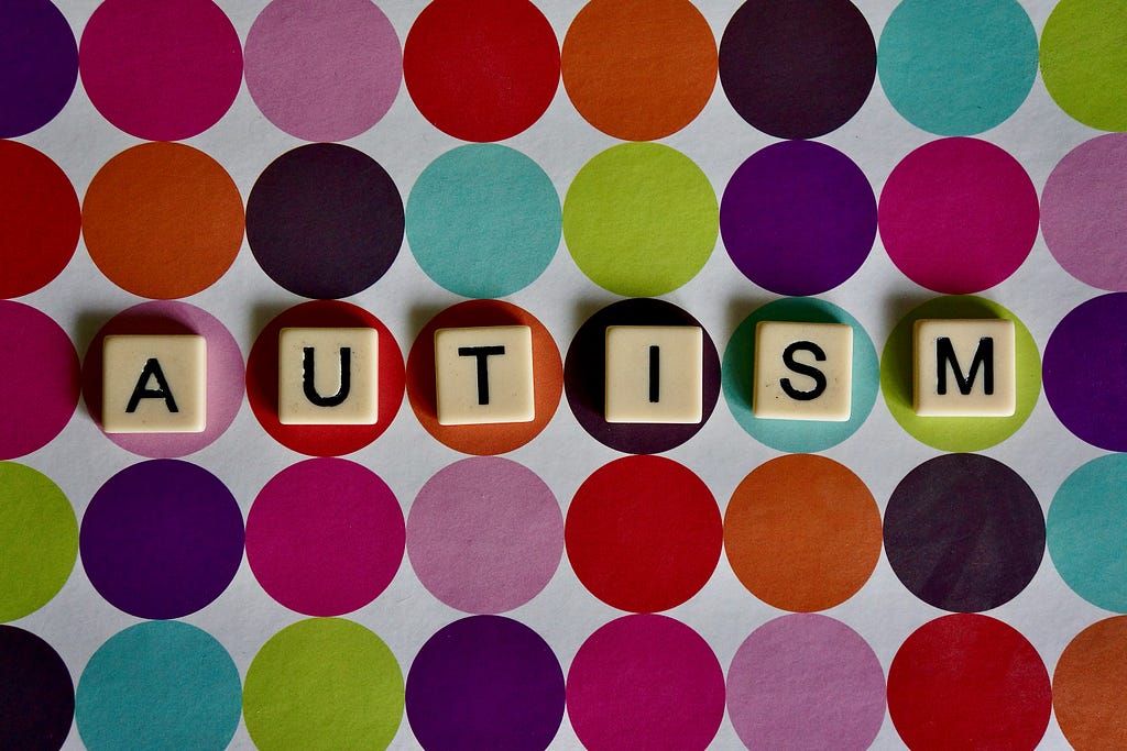 The word AUTISM is written in the square blocks at the front, with the colorful circles in the background.