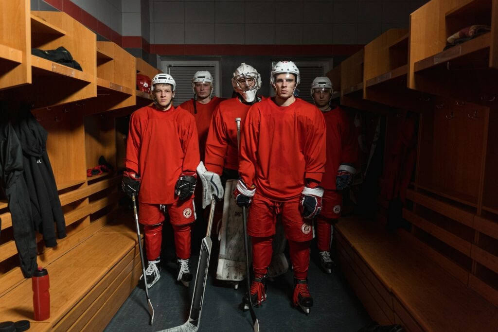 Five somber looking hockey players standing in an empty locker room. Image courtesy of Tima Miroshnichenko at Pexels.
