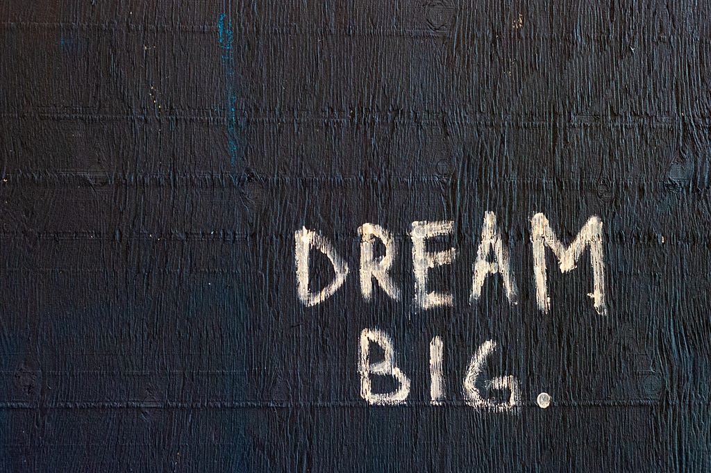 A photo of a dark textured wall with the words “Dream Big” written on it in large block letters.