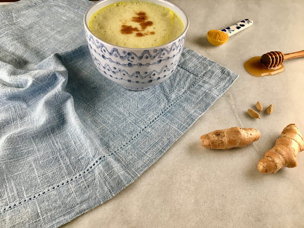 Cup of golden milk surrounded by turmeric and other herbs