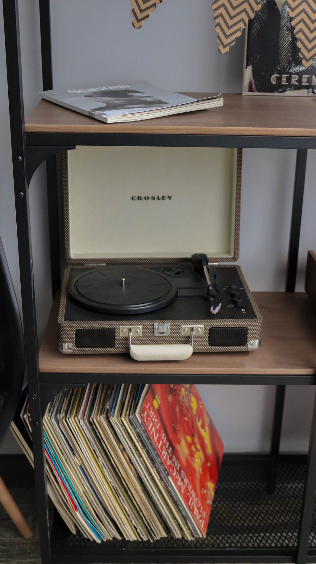 Old record player on a middle shelf with multiple vinyl records below and a book above