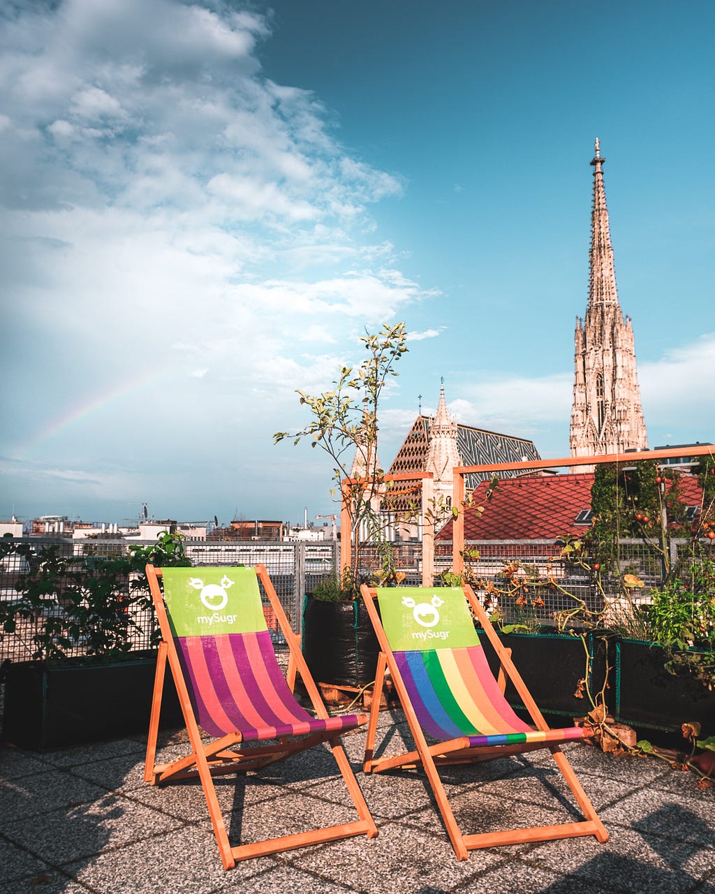 Picture of the from the rooftop terrace, with two colourful deck chairs. Church in the background and a rainbow in the sky.