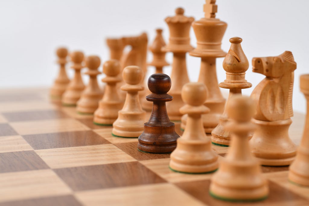 A set of white chess pieces with one lone black pawn in the middle of the front row.