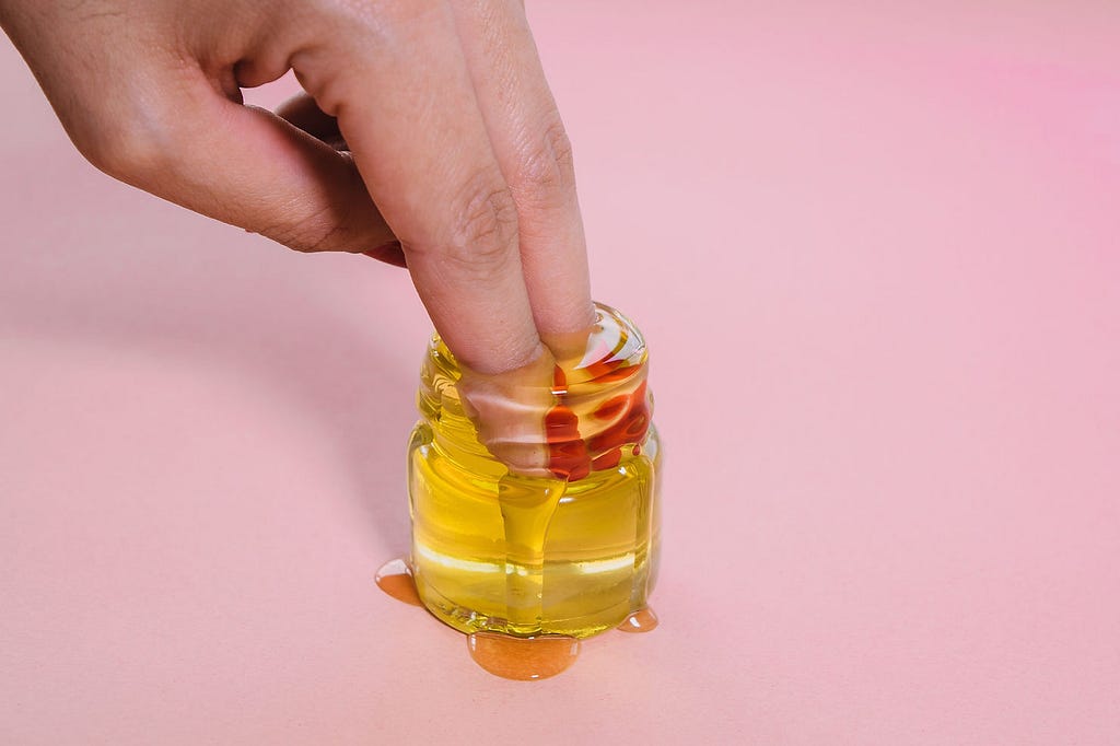 Woman putting two fingers into a jar of cuticle oil with a rose inside of it.