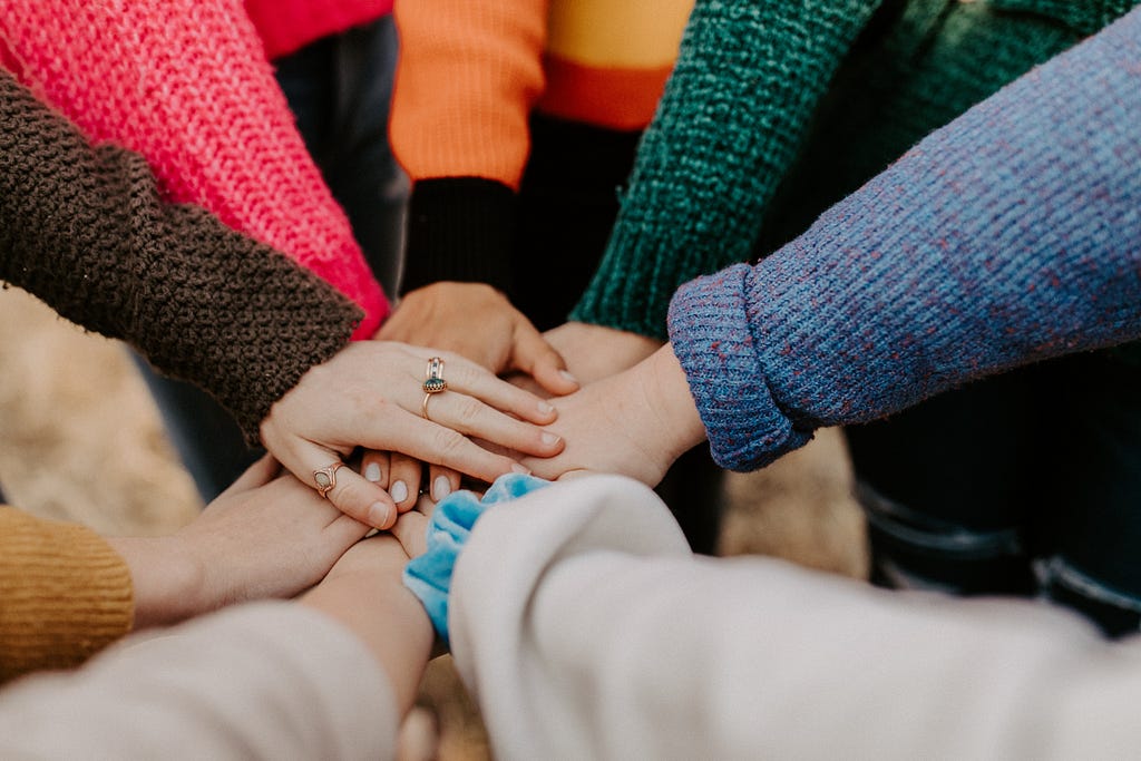 Several hands with various coloured sleeves coming together in the centre of a circle.