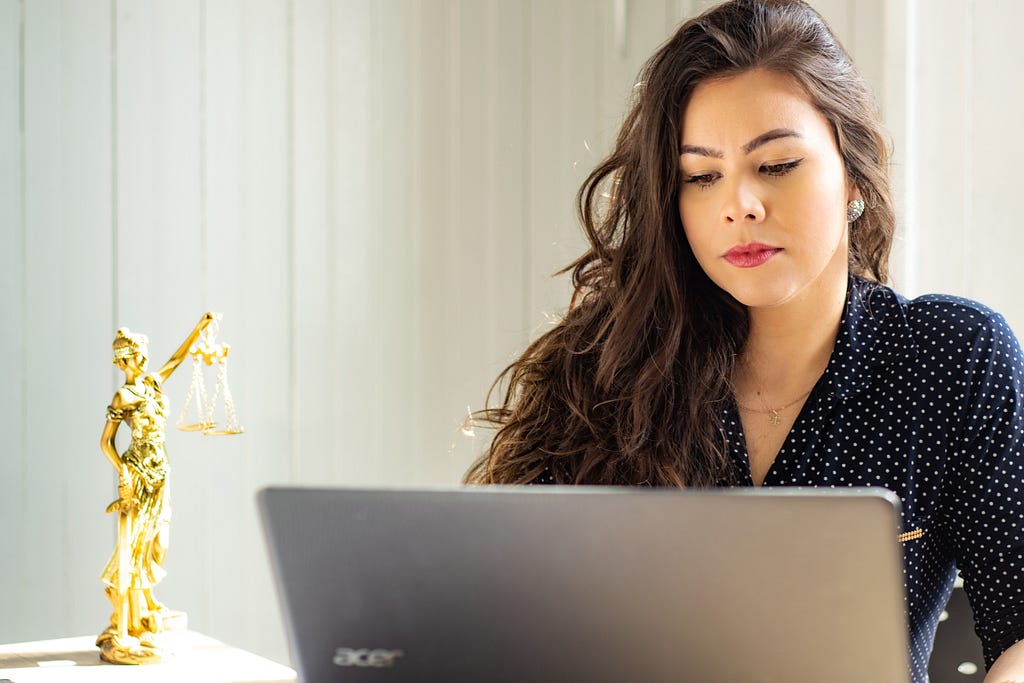 A light-skinned woman with long brown hair working on a laptop