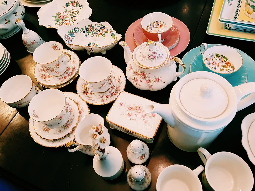 many teacups and tea accoutrements (teapots, saucers, etc) over a table.