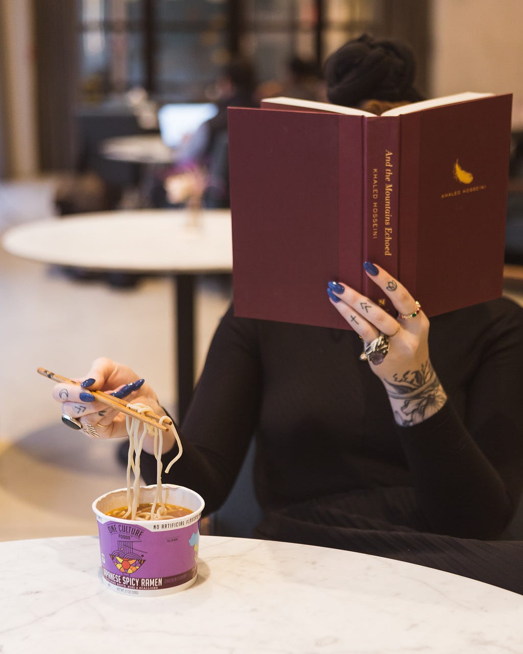 woman sitting reading a book and eating noodles