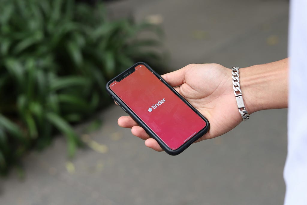 Hand holding a phone opened to the Tinder dating app