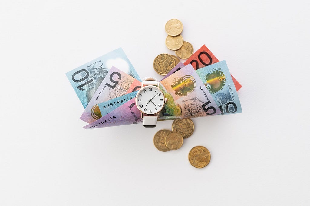 A white watch holding a bunch of Australian currency (notes) with some gold coins scattered on the table.