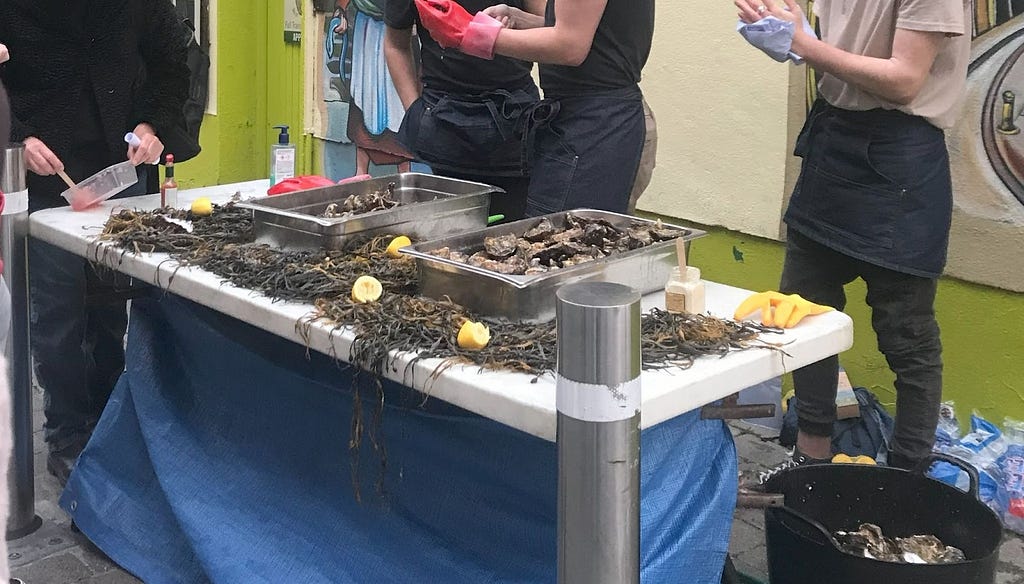 An oyster stall. There are staffs behind the booth wearing gloves, ready to collect the oysters for customers.