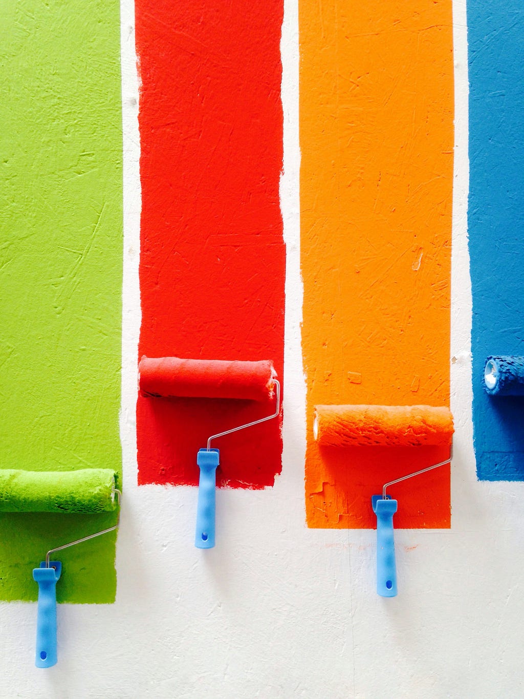 Four paint rollers, each rolling a different color, green, red, orange, and blue